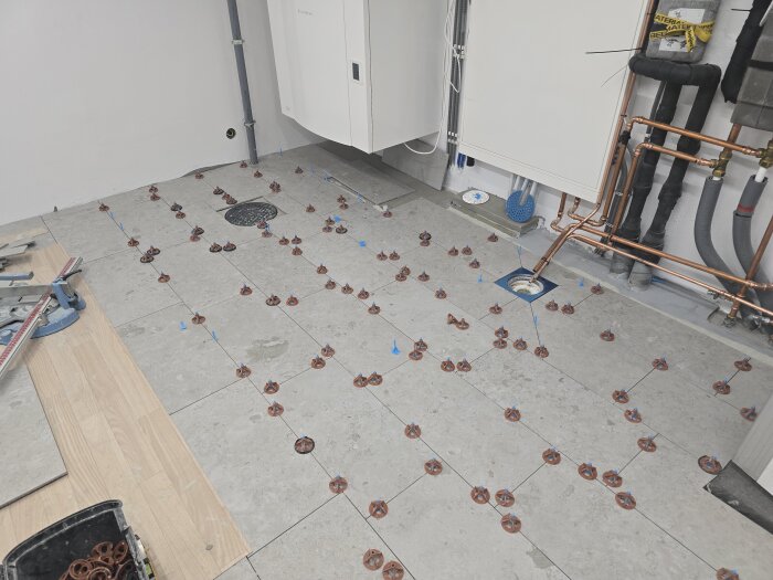 Klinkergolv under installation med nivåjusterare, kopparrör synliga längs väggen i ett duschrum, del av byggprojekt i april 2025.