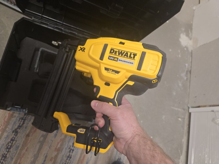 En person håller i en gul Dewalt dyckertpistol framför en svart förvaringslåda.