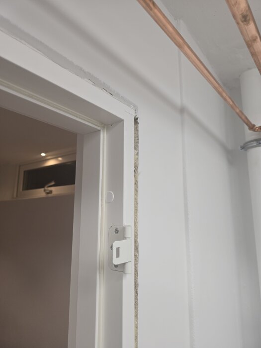 Vit dörrkarm med inspektionslucka och synligt kopparrör ovanför, del av pågående renoveringsprojekt.