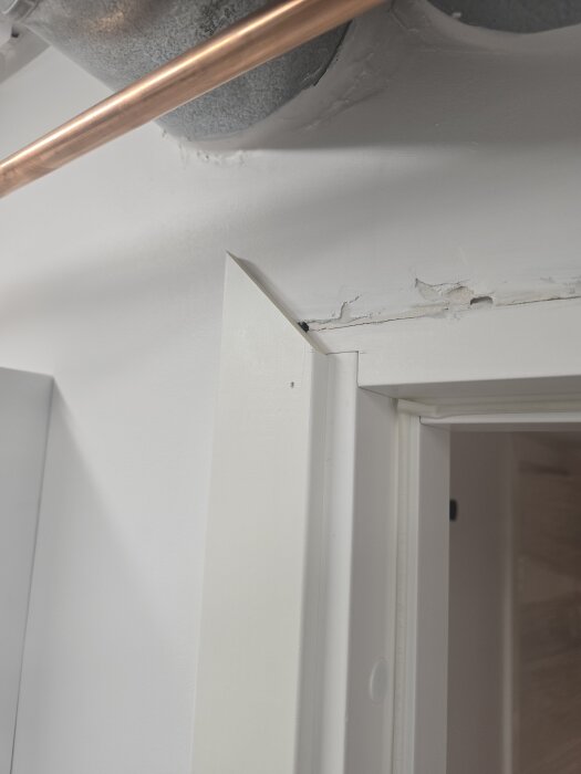 Närbild på dörrfoder i fel nyans, 0502Y istället för 0500N, med små skador på väggen ovanför. Ett kopparrör syns i taket ovanför.