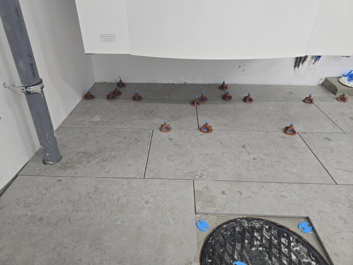 Golvyta med nylagda klinkerplattor och inspektionslucka. Kakelverktyg är placerade på plattorna nära ett rör.