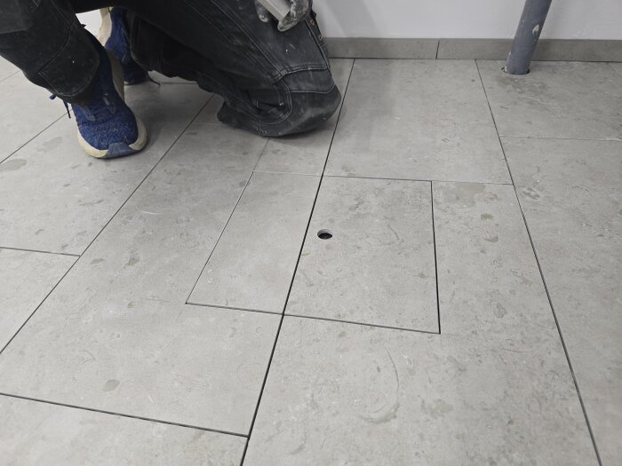 Person i arbetskläder arbetar med klinkergolv med inspektionslucka i samma höjd för snygg finish. Rummet används för projekt med FTX-aggregat och rörinstallationer.