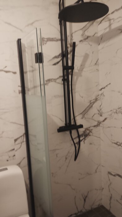 Duschområde med svart duschmunstycke och vit marmorerad vägg i badrum.
