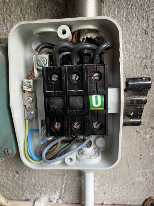 Elektriskt kopplingsutrymme med flera svarta och färgade kablar, inklusive jordkabel, anslutna i en elbox på väggen.