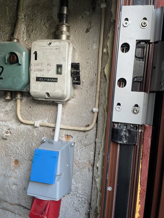 Tre fasuttag med blått och rött lock monterat på vägg; kopplingsbox märkt "Elpanna" syns bredvid. Viss isolering och kablar synliga runtom.