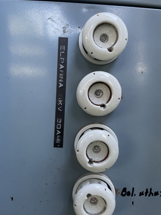 Tre porslinsproppar monterade på en grå plåtpanel, märkt "ELPANNA GKV 20AMP".