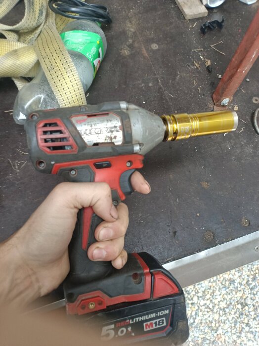 Borrmaskin med röd-svart handtag och M18 lithium-ion batteri, hålls i en hand på ett arbetsbord med verktyg.