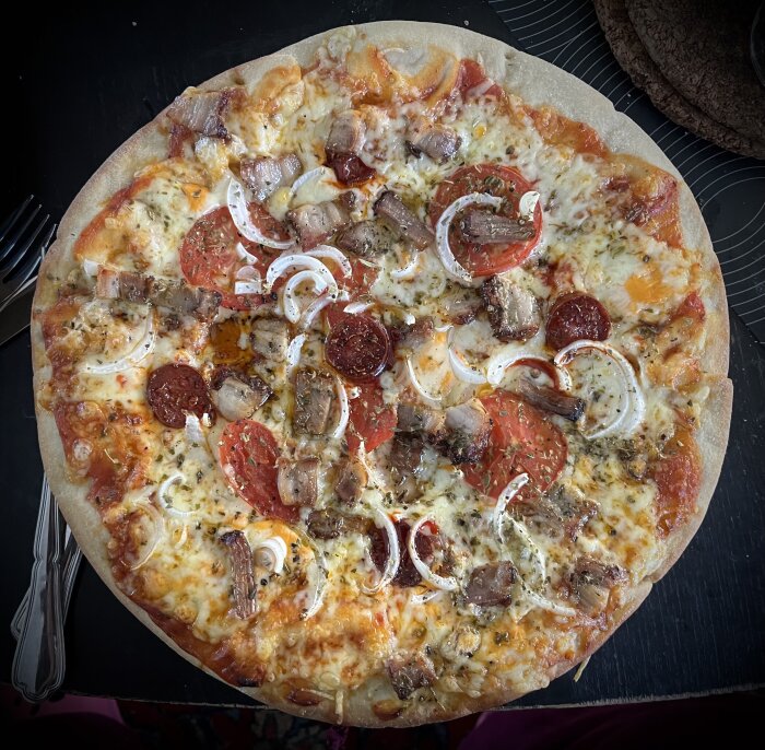 Hemlagad pizza med tomatskivor, färsk lök, porchetta, chorizo, ostsås, tomatsås, riven ost, oregano och svartpeppar.