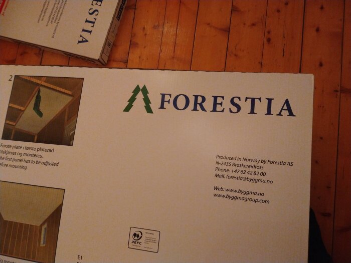 Förpackning med Forestia-panel för takinstallation, med instruktioner, kontaktuppgifter och PEFC-certifiering. Ligger på ett trägolv.