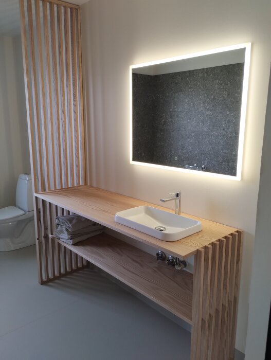 Egen designad badrumsmöbel med bänk och spegel i trä, handfat och plats för förvaring, belyst spegel ovanför.