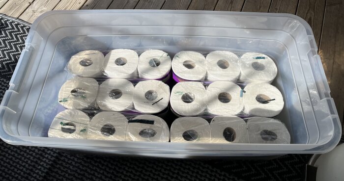 Plastlåda fylld med staplade förpackningar av toalettpappersrullar, 54 rullar totalt.