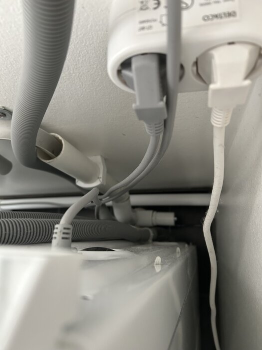 Öppet avloppsrör i samband med andra elkablar och slangar under en diskbänk.