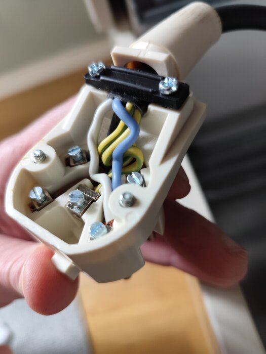 Öppen stickkontakt med synliga elkablar i blått, gult och grönt, samt skruvar som håller dem på plats.