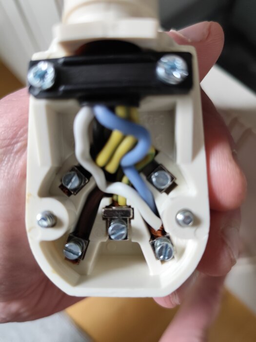 Närbild av en stickkontakt med synliga färgade kablar, blå, gul/grön, vit och brun. Skruvar och anslutningspunkter syns tydligt.