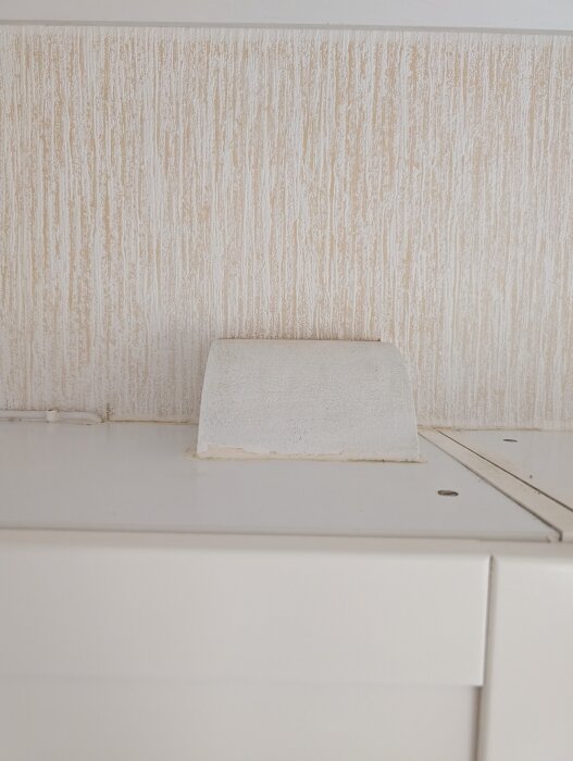 Ventilationsutlopp i ett rum med strukturtapet, en vit skiva syns under, där luften leds genom väggar, förklarat i inlägg.