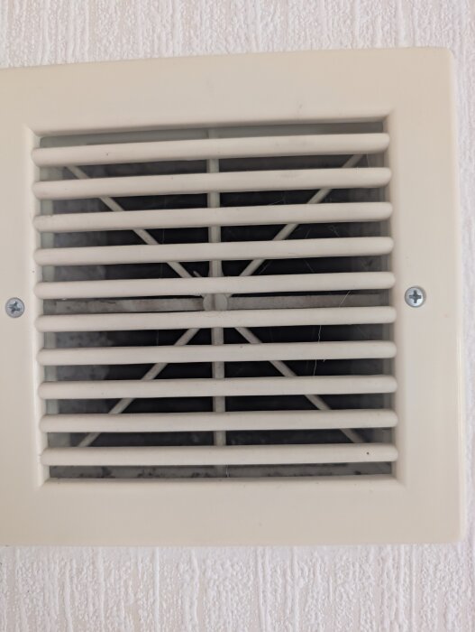 Ventilationsgaller monterat på en vägg av strukturtapet med smuts och damm mellan gallren.