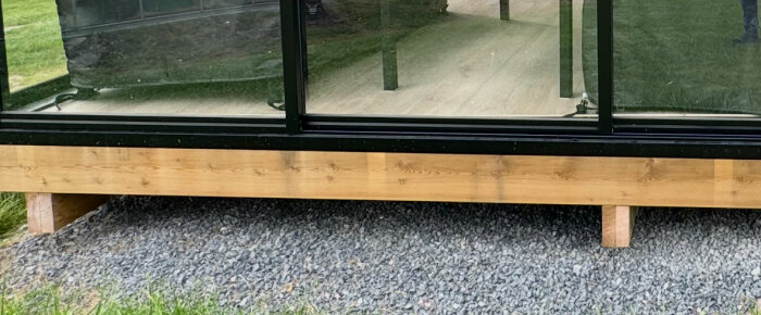En trykkimpregnert bjelke på et uterom med svart plåt festet for estetisk effekt, plassert over grus. Spørsmål om bruk av syllpapp mellom plåt og bjelke.