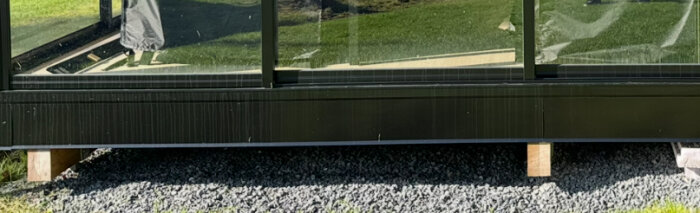 Svarte metallplater montert på siden av en trykkimpregnert bjelke på et uterom med grusdekke nedenfor.