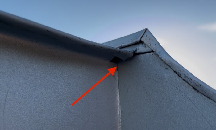 Röd pil pekar på en skarv i plåt där misstänkt regnvatten tränger in.