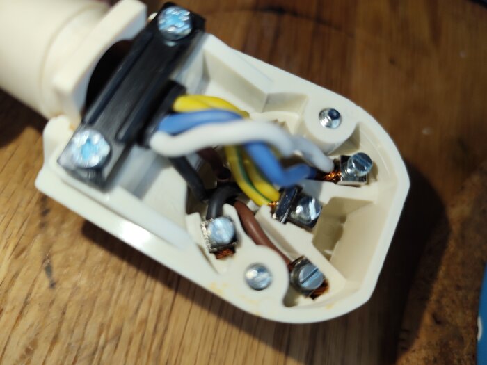 Elektrisk anslutning med gröngula, bruna och svarta kablar fästa vid skruvar i en plastkontakt, några kablar är uppvikta.