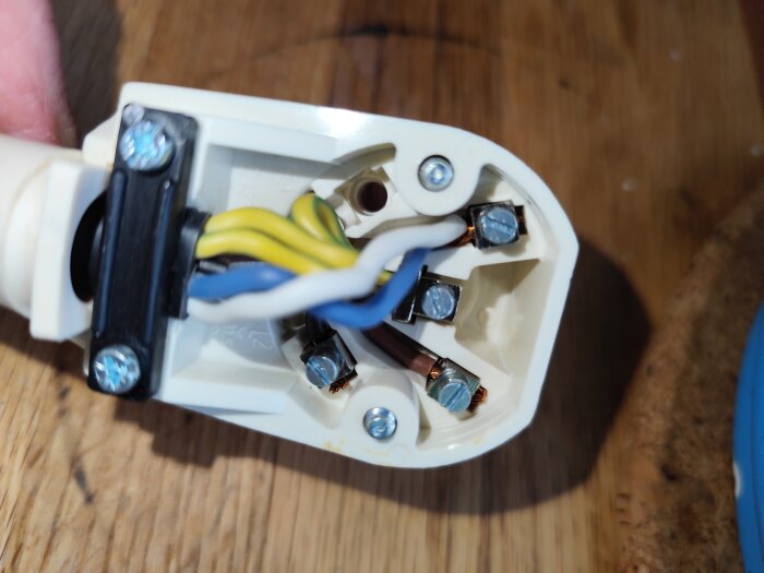 Närbild av en elektrisk kontakt med synliga gröngula, blå, vita, bruna och svarta kablar anslutna till skruvplintar.