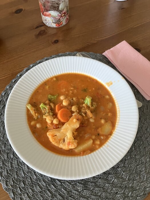 Linsgryta med blomkål, morötter och broccoli serverad i en vit tallrik på en flätad bordstablett.