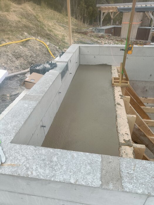 Gjuten betongstruktur för ett spabad, omgiven av träformar och arbetsmaterial, med en byggnad i bakgrunden under ett byggprojekt.