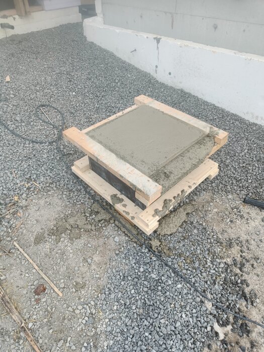 Nyss gjuten betongplatta med form av trä, placerad på grusig mark, en del av ett spabadprojekt.
