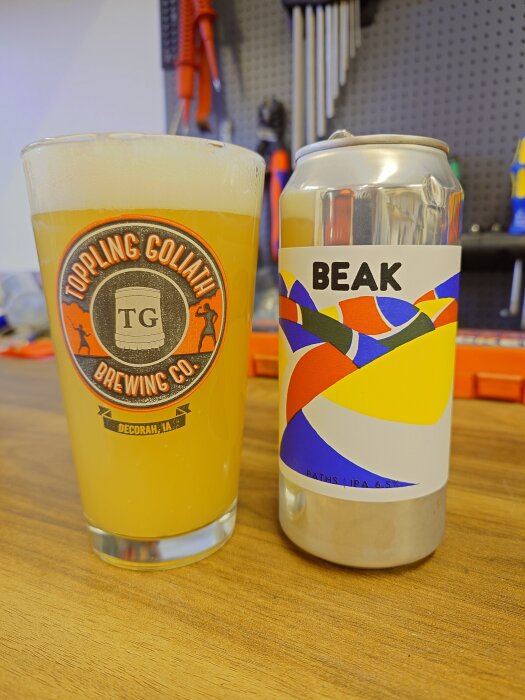 Glas med öl från Toppling Goliath och burk från Beak på ett bord, med verktyg i bakgrunden.