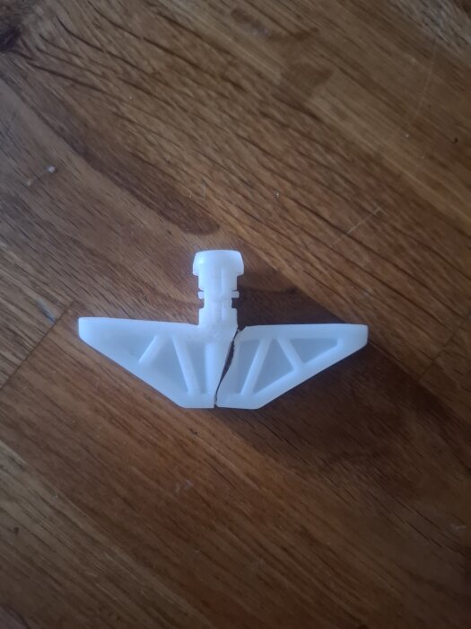 Brutet plastfäste från wc-stol cistern liggande på ett trägolv.