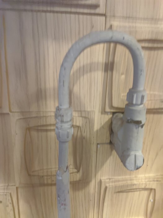 Läckande vattenutkastare med kopplingar i ett garage. Rörledningarna är delvis synliga och visar en bockat kopparrör och ett prisolrör.