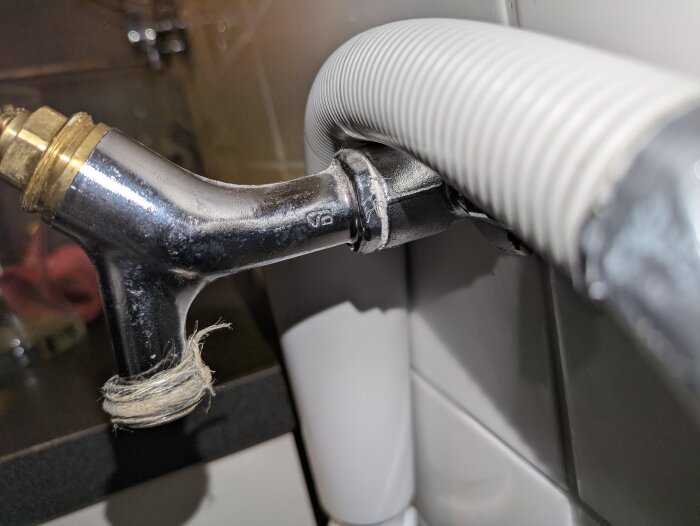 Ventilöverstycke i metall med fäste för anslutande slangar och synlig gängtejp, installerat under en diskbänk.