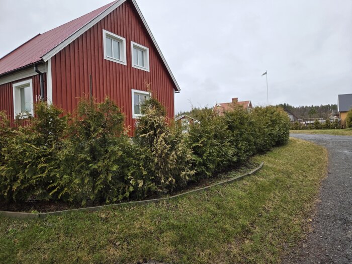 Rött hus med vita knutar och omgivande häckar, sett vid en grusväg och gräsyta, diskuterat som "problemområdet" för gödsling.
