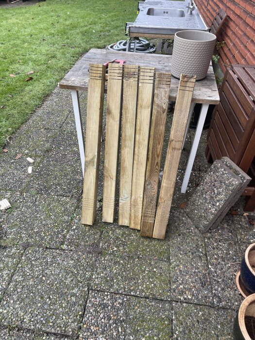 Sågade trästolpar och reglar på ett bord i trädgården, med en rostfri diskbänk och tegelfasad i bakgrunden.