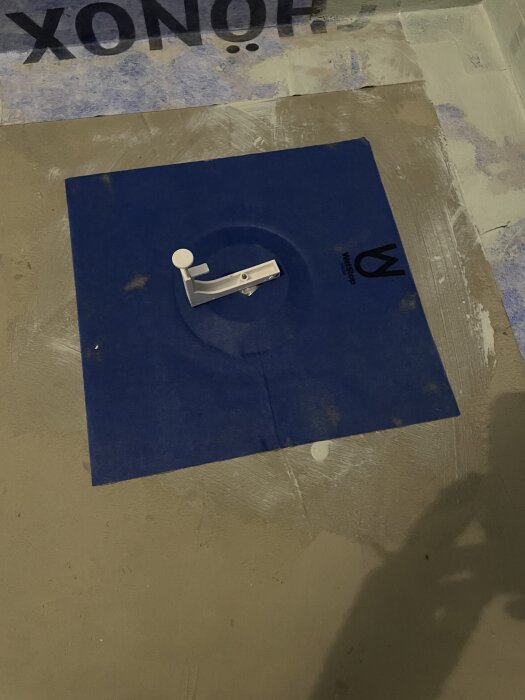 Byggplats med blå vattenavstängare installerad på golvet, omgiven av grå betong och väggisolering.