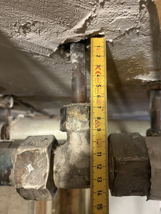 Kopparrör med T-koppling och mäts upp till 6-7 cm synlig ovanför tak, bredvid ett måttband.