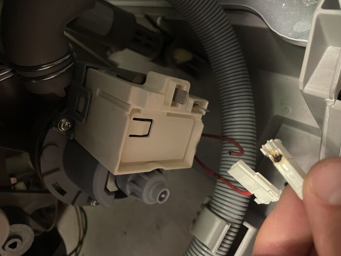 Bränd kontakt på elektrisk pump med anslutna kablar, visas i närbild; en hand håller den trasiga kontaktbiten.