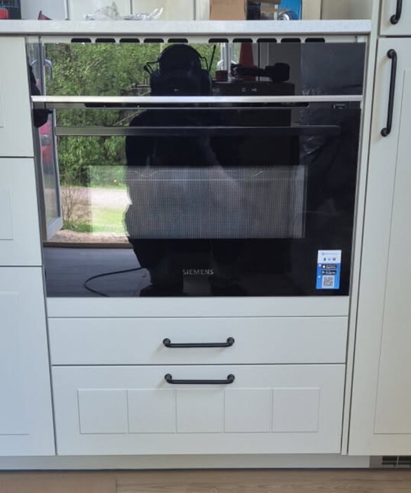 Inbyggd Siemens ugn i ett modernt kök, omgiven av vita skåpluckor och svarta handtag.
