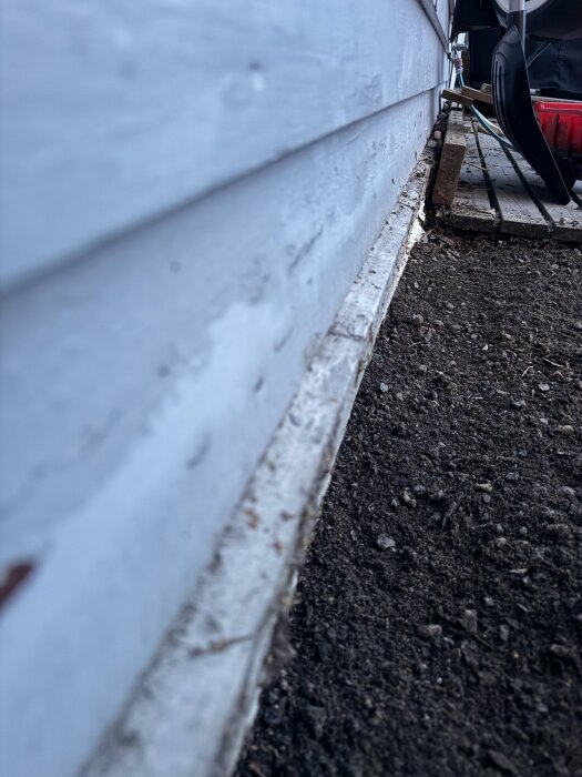 Närbild av nedersta brädan på fasaden, genomrutten och behöver bytas. Fjällpanel ovanför, avslut mot betongplatta.