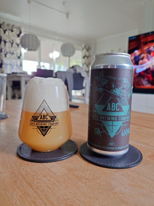 Ölglas och burk från Apex Brewing Company står på ett bord, etiketten visar en stiliserad dödskalle och texten "IPA 6.5%".