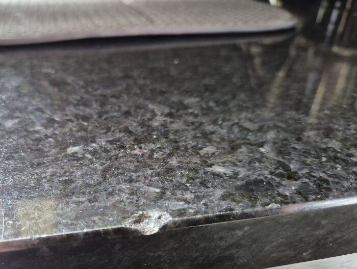 Flisa borta från mörk stenskiva i kök närbild.