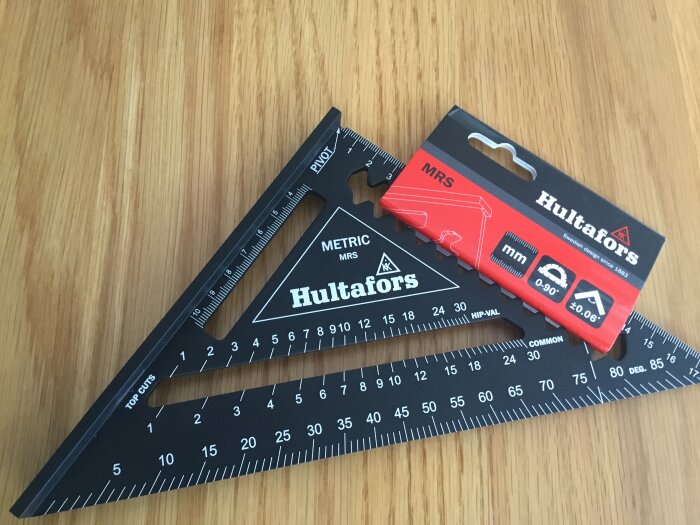 Svart Hultafors vinkelhake och röd förpackning på ett träbord.
