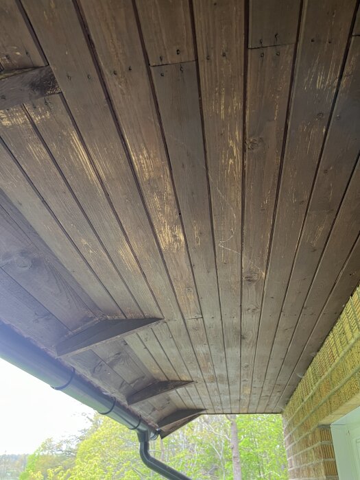 Takutsprång av trä med renovering påbörjad, där ytan är delvis tvättad med Jape målartvätt, för en förändring från brun till grå.