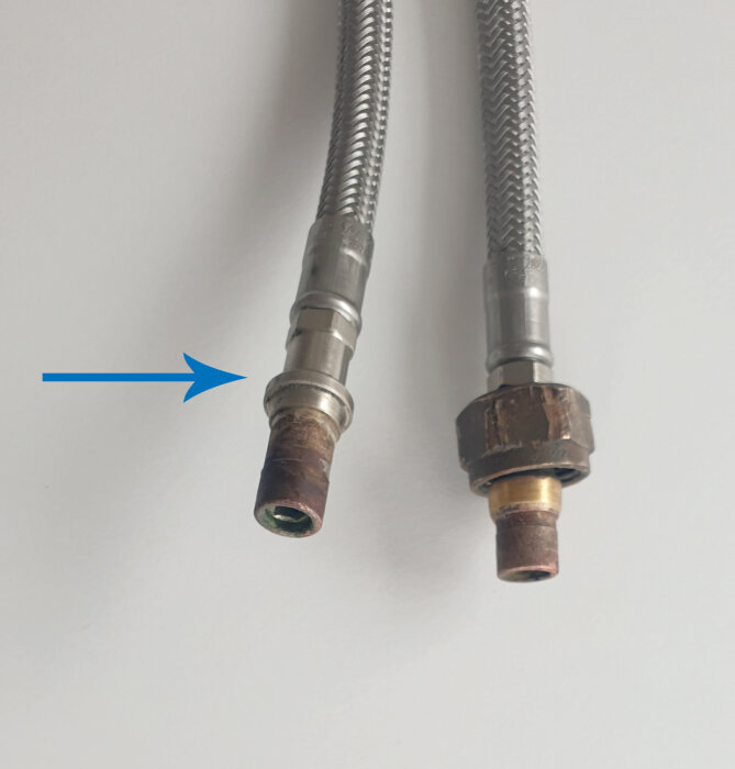 Två köksblandar-slangar, den vänstra med en trasig ände och en lossnad nippelring, pil pekar på skadan.