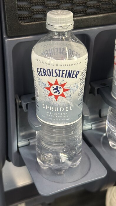 Flaska med Gerolsteiner kolsyrat mineralvatten i en dryckeshållare på en tågresa, med text på tyska.