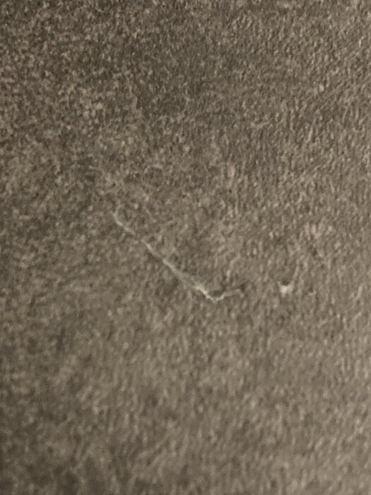 Närbild på en slät, grå yta med en liten spricka eller repa i mitten.