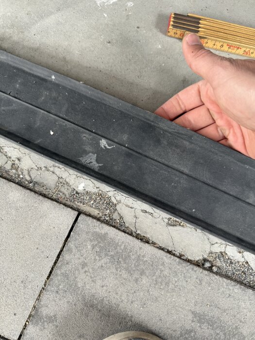 Gummiliknande remsa under syll på betonggolv, hand håller mätsticka och visar placering.