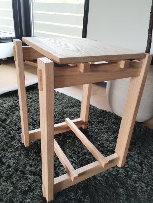 Litet bord av ek med wedgejoints, kilar av bok. Står på grön matta framför fönster.