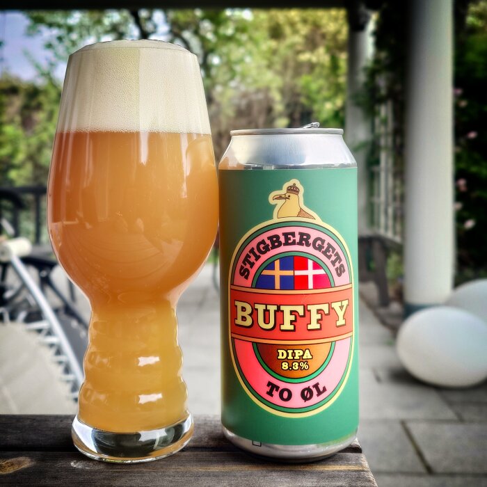Ett glas och en burk öl märkt "Stigbergets Buffy DIPA 8.3%" står på ett bord utomhus.