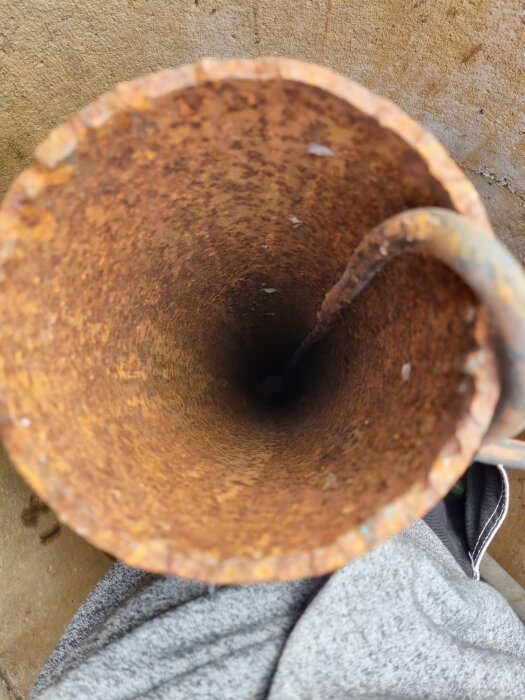 Rostig brunnsöppning med rör och mörkt hål, fotad uppifrån.